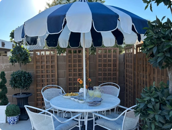 Elegant and stylish outdoor patio featuring the Pagoda Series patio umbrella in a navy and white Sunbrella fabric with a distinctive pagoda cut canopy. This influencer-curated setup highlights a sophisticated dining space with a chic white wrought iron table and chairs, creating a timeless and luxurious outdoor ambiance.