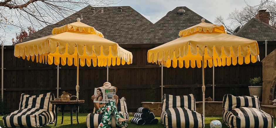 Elegant outdoor lounge featuring the Terrace Series patio umbrellas in a bold yellow Sunbrella fabric with a scalloped valance. This stylish backyard setup blends vintage charm with modern luxury, complemented by striped lounge chairs, a cozy seating area, and a relaxed ambiance perfect for outdoor leisure.