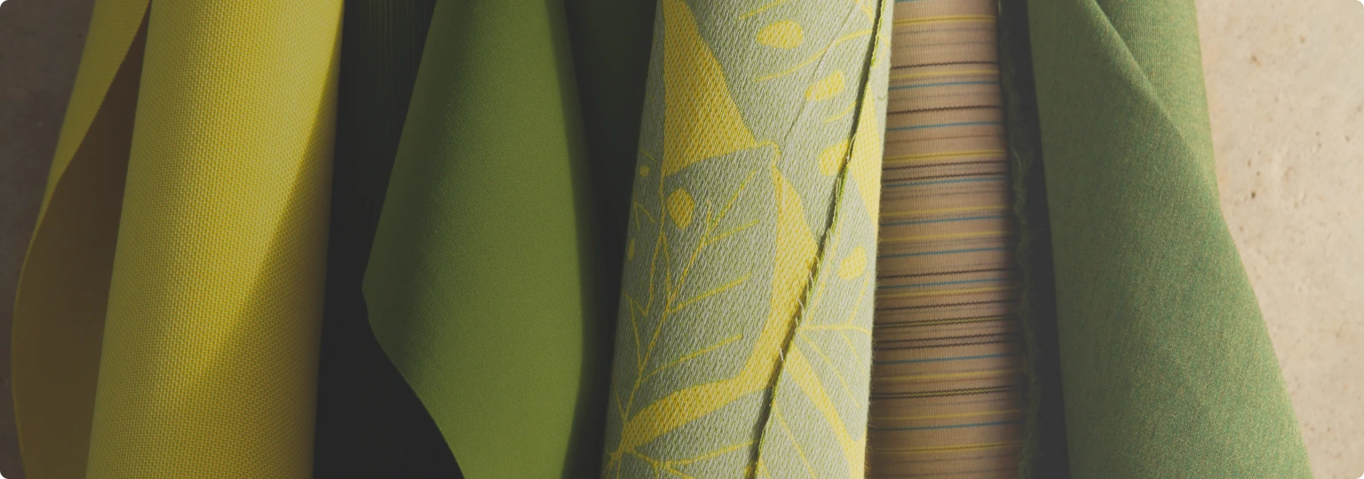 Close-up of premium outdoor umbrella fabrics in various shades of yellow and green, showcasing high-quality Sunbrella textiles for durability and style. Featuring intricate weaves and bold patterns, these fabrics offer versatile customization options for patio umbrellas and outdoor living spaces.