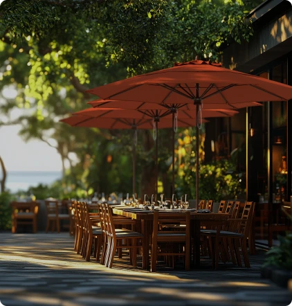 Lifestyle image showcasing the Madera Series Patio Umbrellas by California Umbrella, featuring warm, earthy canopies over outdoor dining tables in a serene, tree-lined setting, highlighting their classic design and robust durability for elegant commercial spaces.