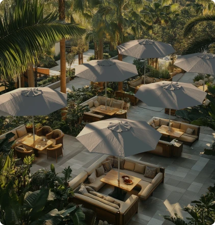 Lifestyle image showcasing the Newport Series Commercial-Grade Patio Umbrellas by California Umbrella, elegantly arranged over outdoor seating areas in a lush tropical setting, highlighting their stylish design and durability for upscale commercial spaces.