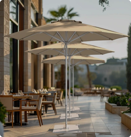 Lifestyle image featuring the Rodeo Series Patio Umbrellas by California Umbrella, elegantly shading outdoor dining tables along a modern walkway, showcasing their sleek design and durability for upscale commercial and hospitality settings.