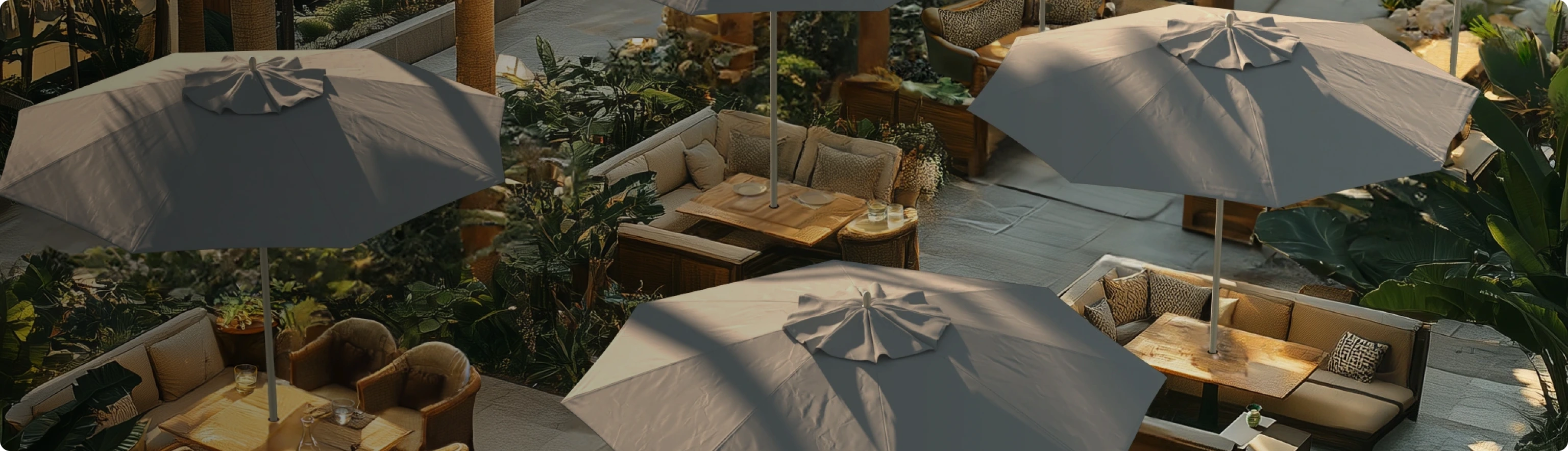 High end outdoor dining space featuring multiple designer patio umbrellas with Sunbrella fabric canopies, providing stylish sun protection. Surrounded by lush greenery and elegant seating, these commercial-grade patio umbrellas create a sophisticated ambiance for high-end restaurants, resorts, and outdoor lounges.